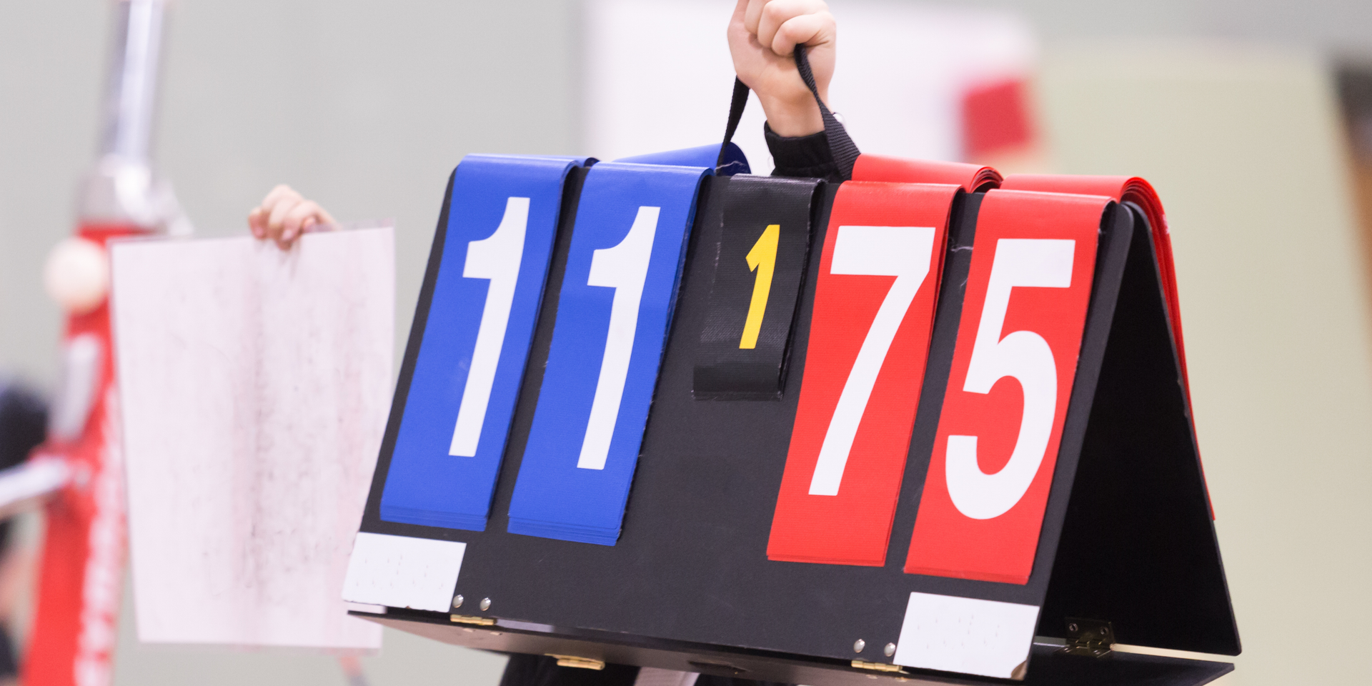 A gymnastics  judge is holding a scoreboard that says 11 75