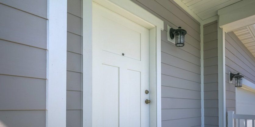 Hardy Plank Siding — Front Door of a Home with a Lamp on the Gray Siding in Clayton, NC