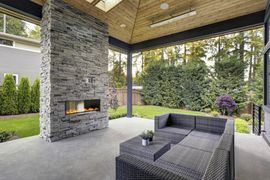 Concrete Patios — Modern Home Features a Backyard with Covered Patio Accented with Stone Fireplace in Clayton, NC