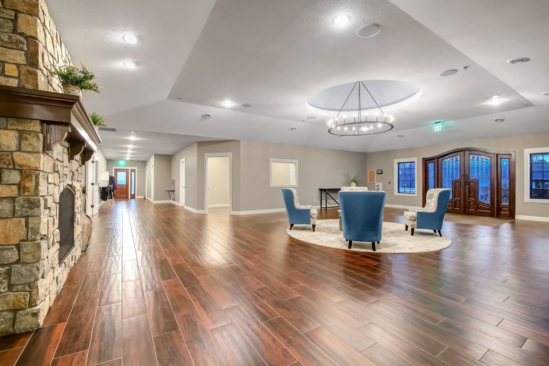 A large room with hardwood floors , chairs , a fireplace and a chandelier.