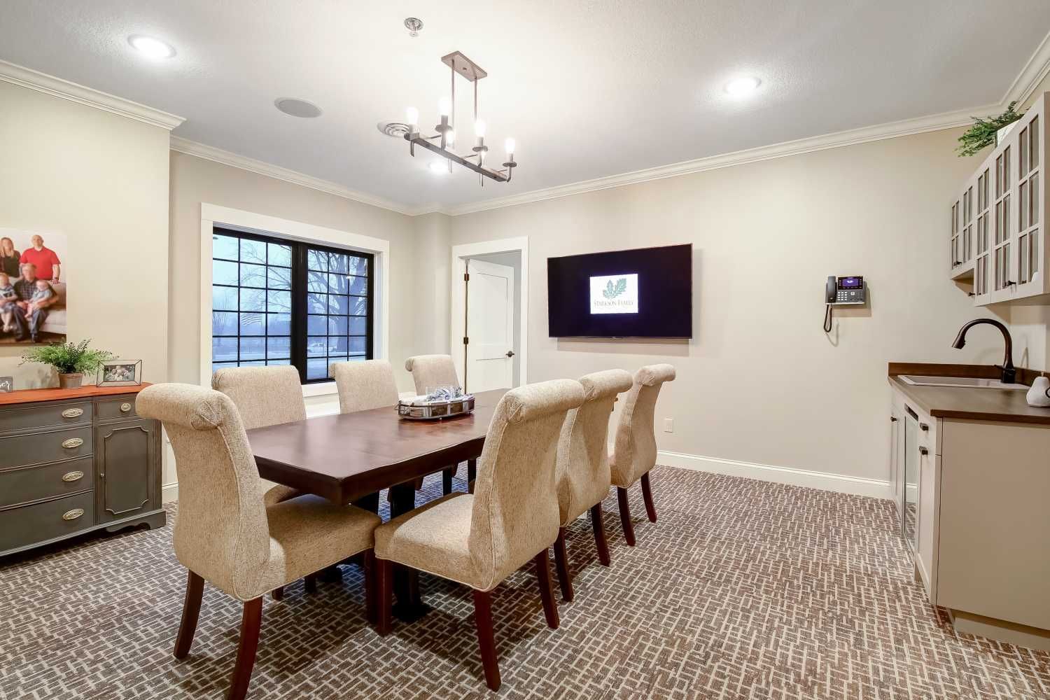 A dining room with a long table and chairs and a flat screen tv.