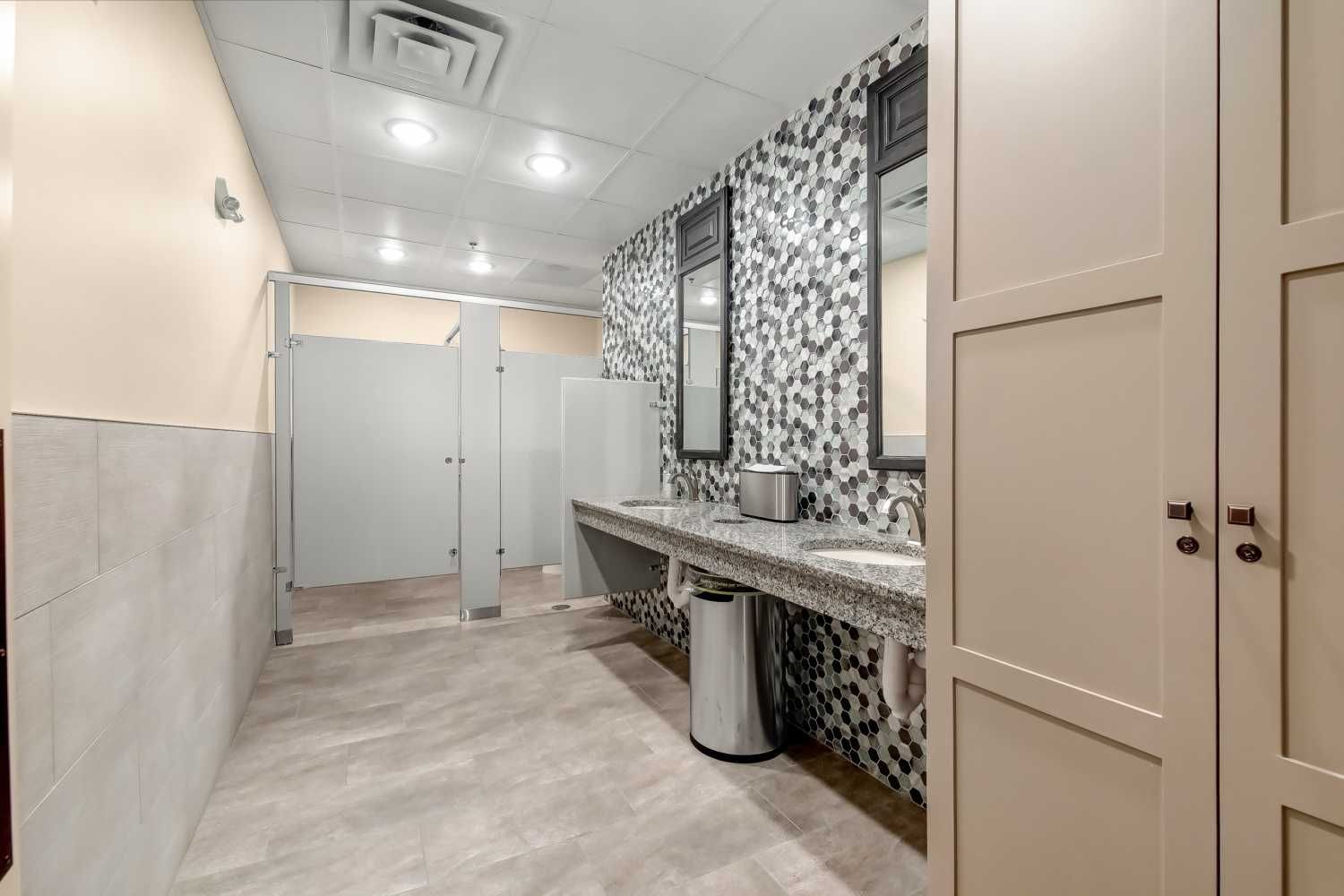 A bathroom with two sinks , two mirrors and a trash can.