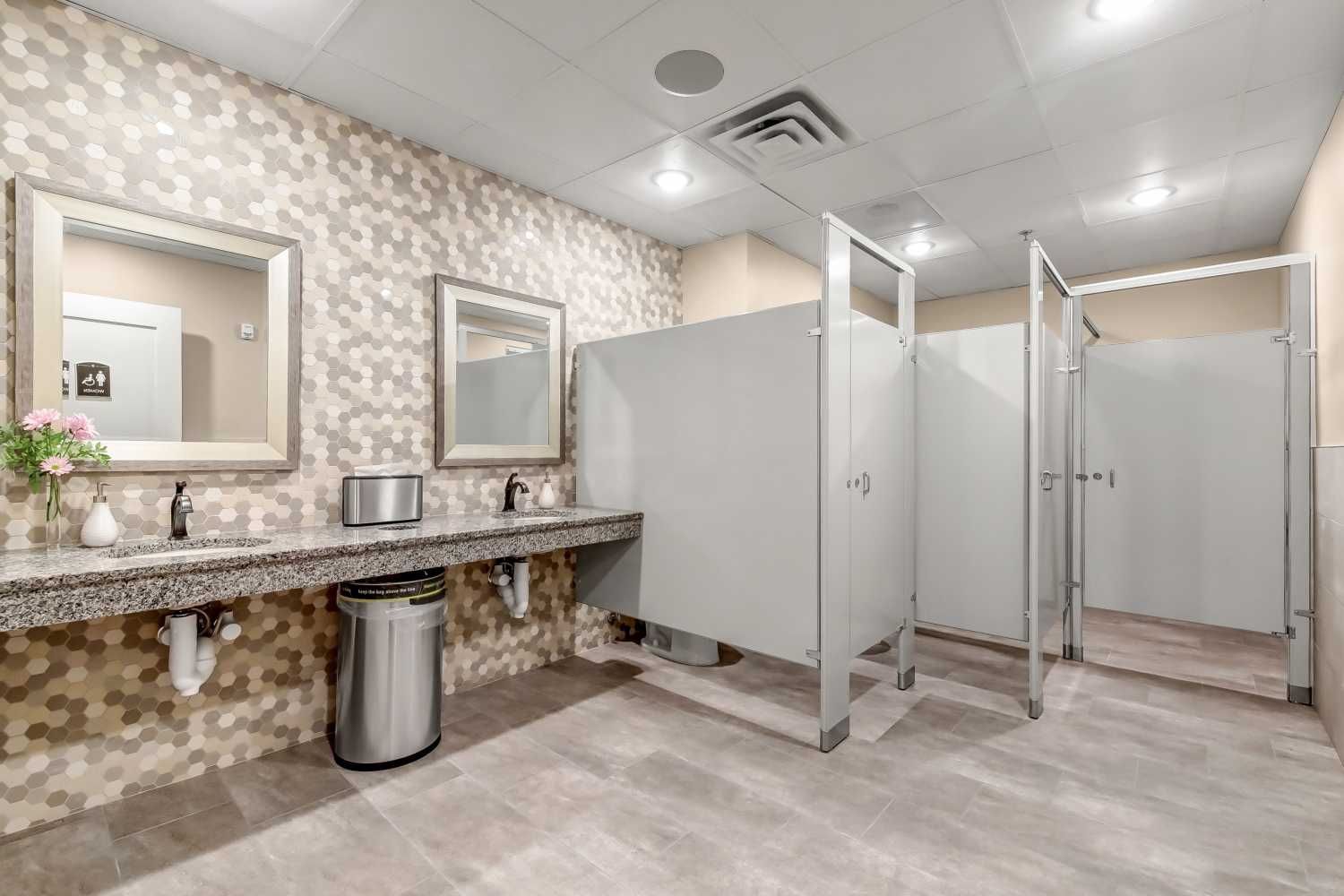 A public restroom with a sink , mirrors and a trash can.