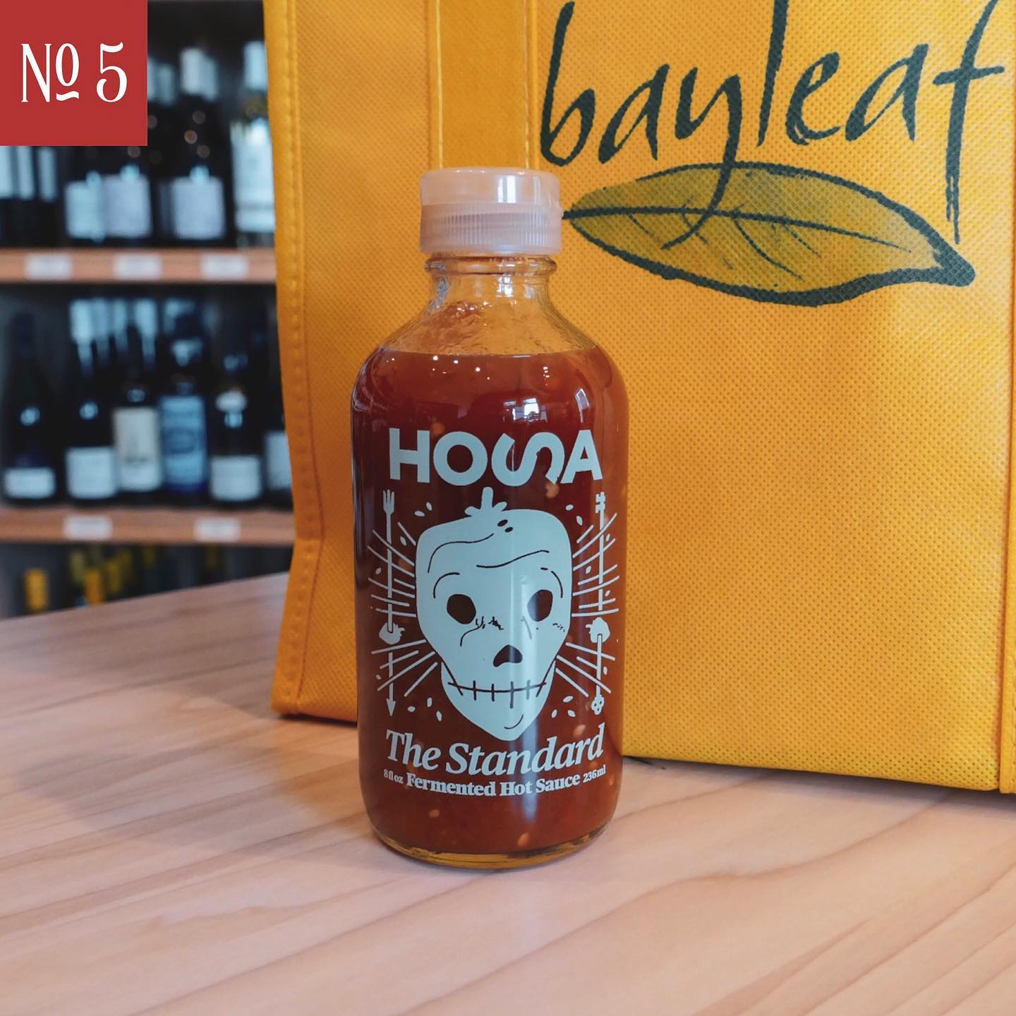 a bottle of hossa hot sauce next to a yellow bayleaf bag