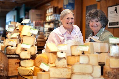 two women are standing in front of a pile of cheese .