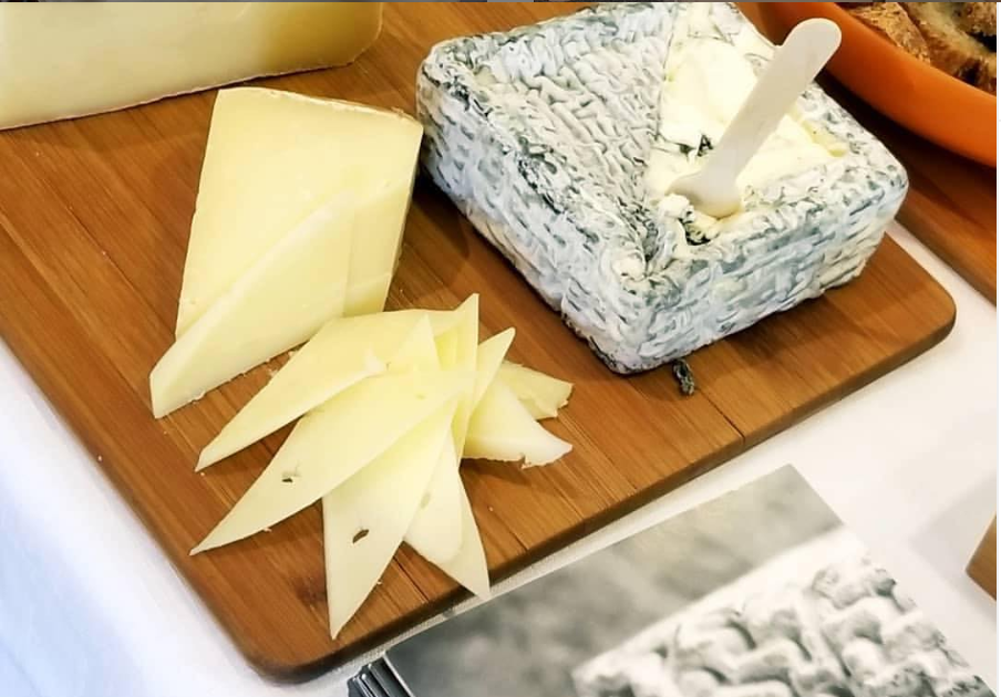 a wooden cutting board with cheese and a spoon on it