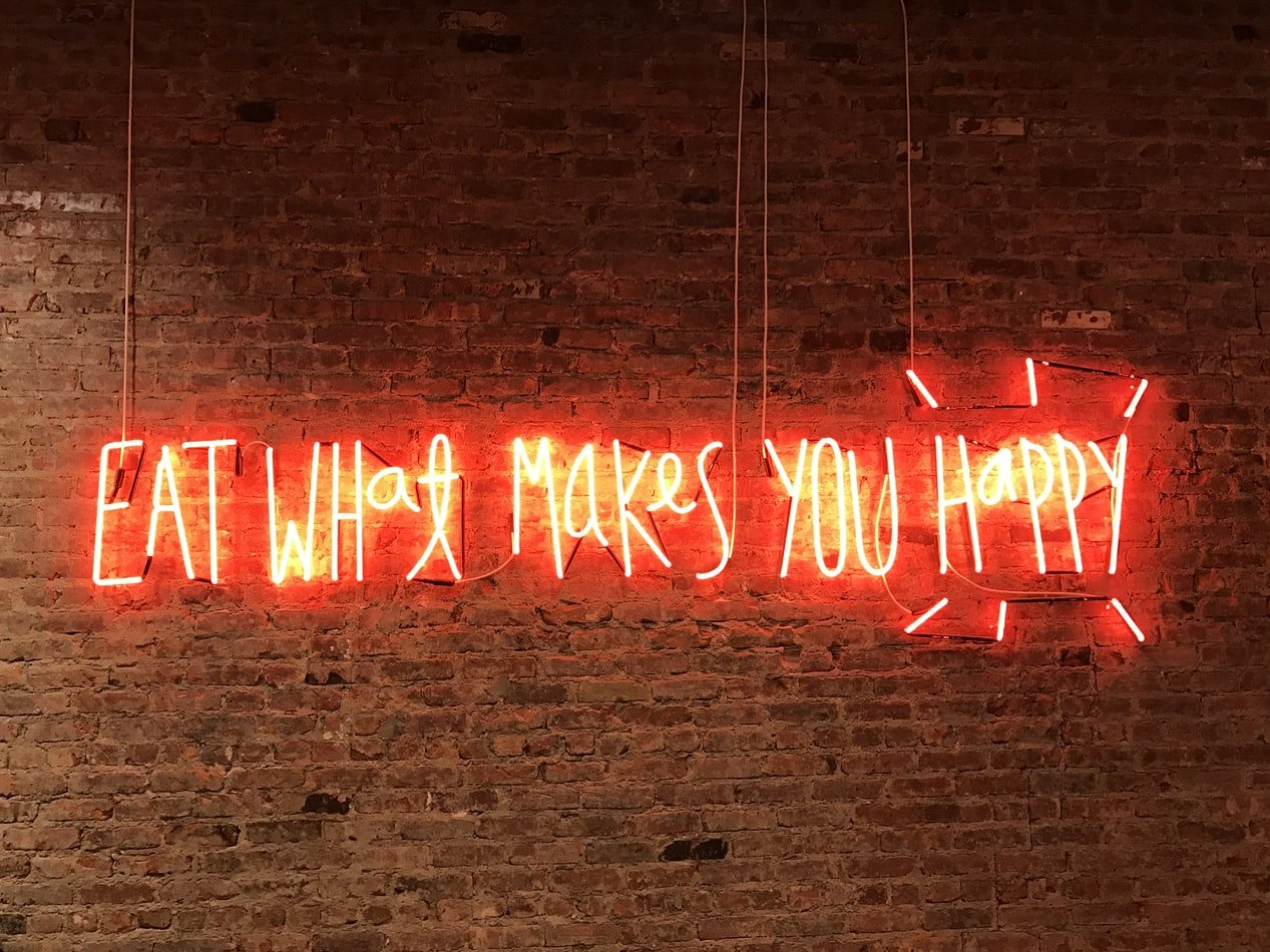 a neon sign on a brick wall that says eat what makes you happy