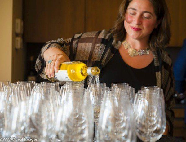 a woman is pouring wine into a row of wine glasses