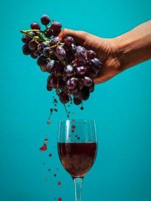 a hand is holding a bunch of grapes over a glass of red wine .