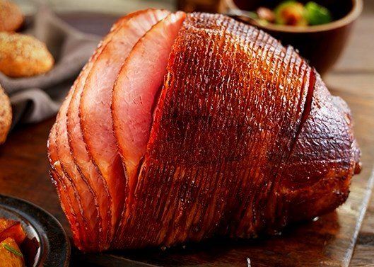 a large piece of ham is sitting on top of a wooden cutting board .