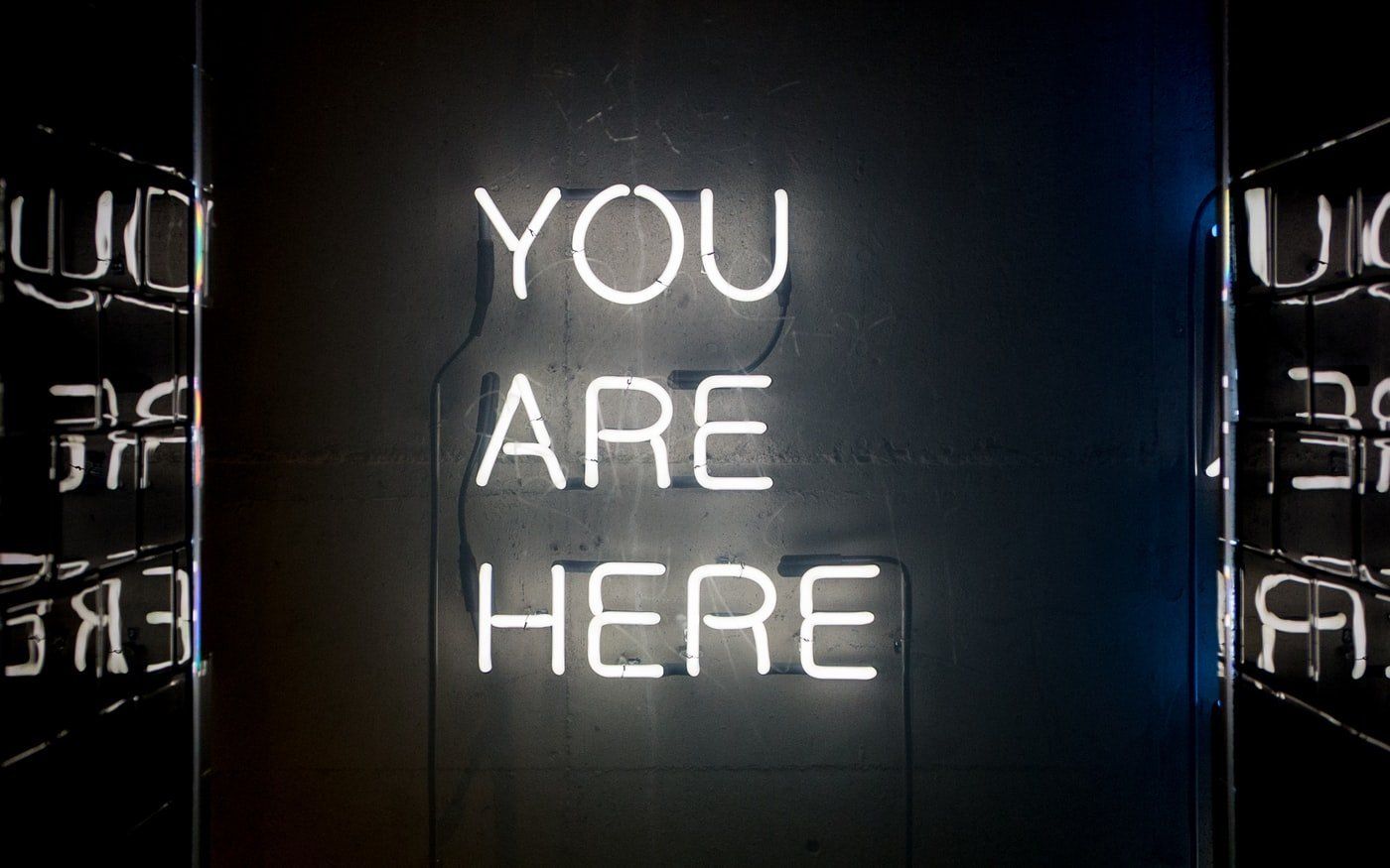 a neon sign that says `` you are here '' is hanging on a wall .