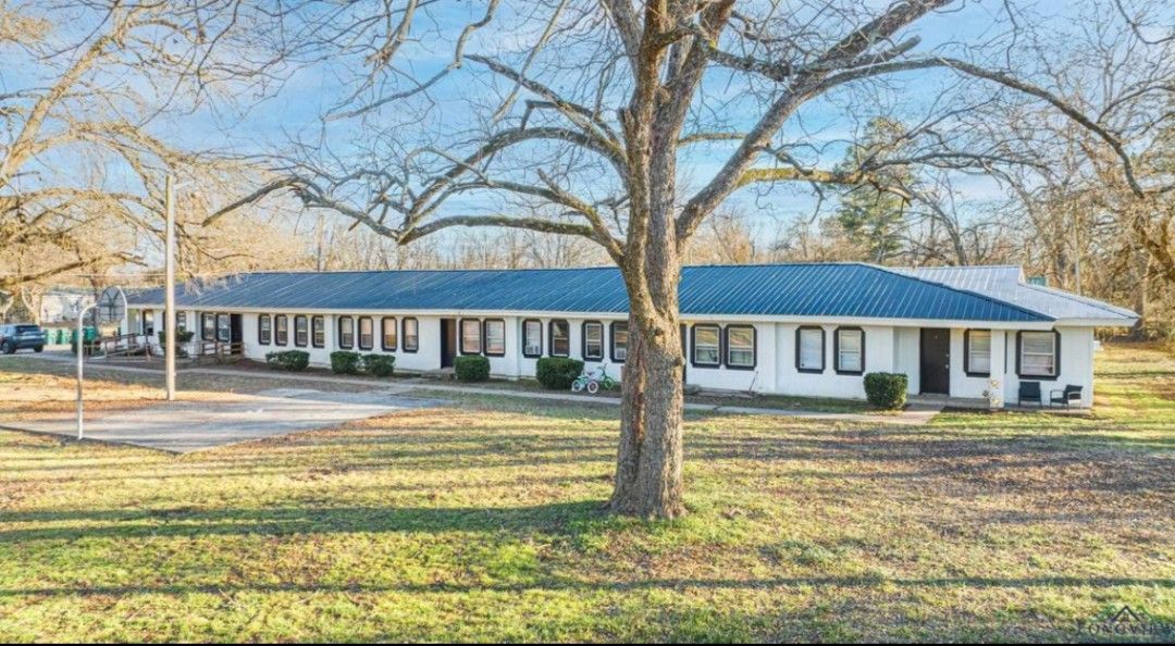 A small, gray house with a black door and large windows, surrounded by green grass and a concrete driveway.