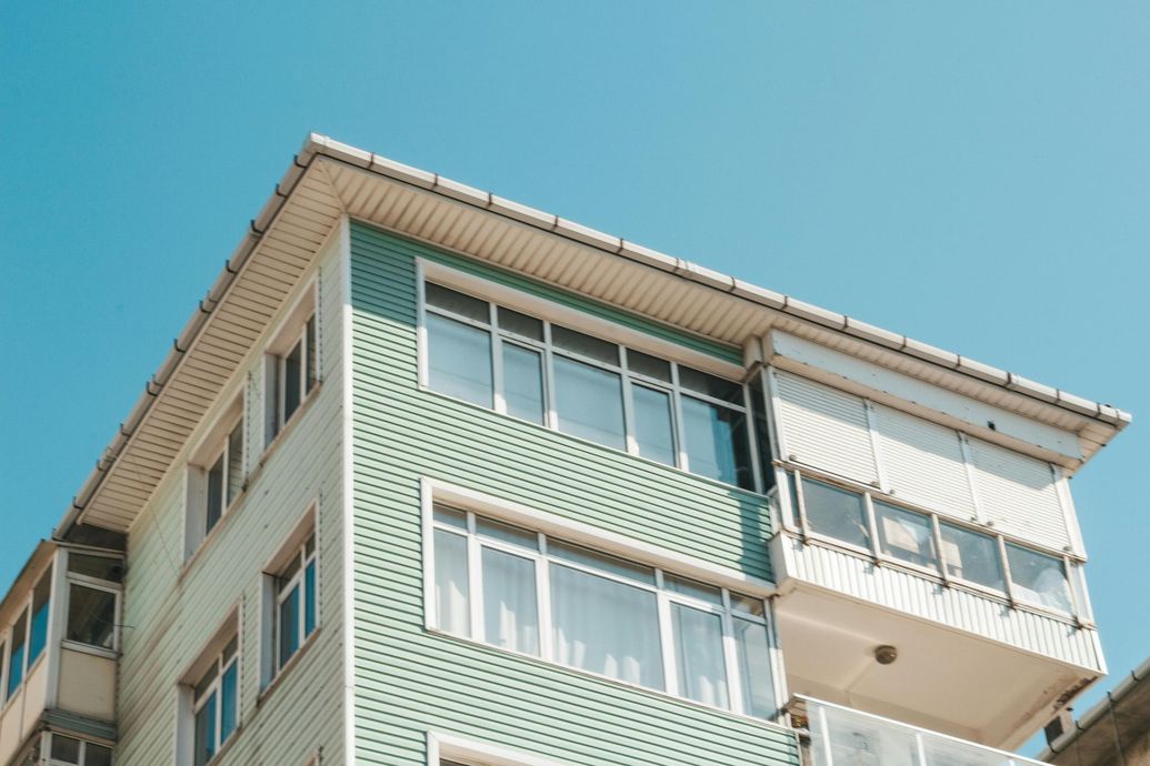 Multi-story building with teal siding and white window frames against a clear blue sky.