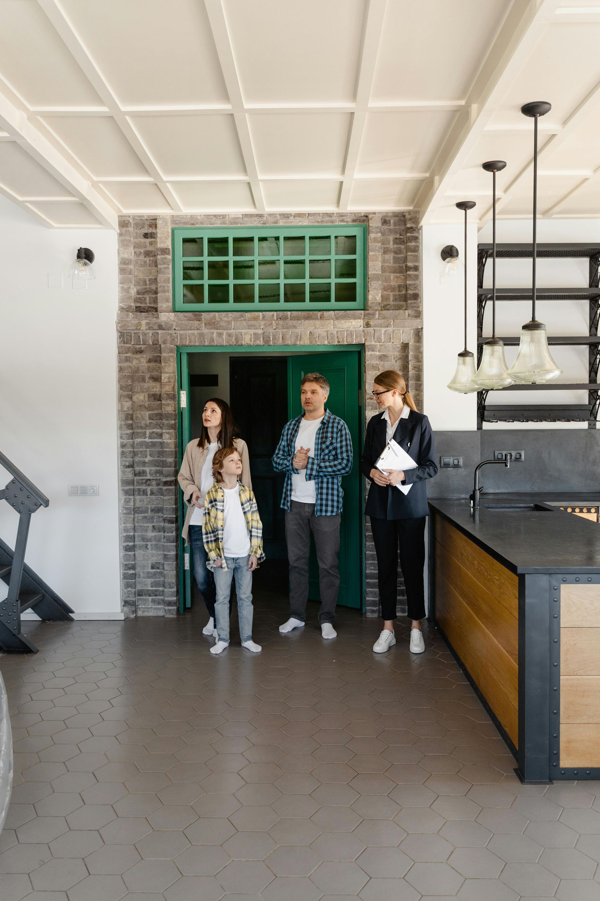 Family looking at a home with a realtor. Inside a room with a brick wall, green door, and kitchen.