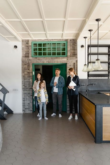 Family looking at a home with a realtor. Inside a room with a brick wall, green door, and kitchen.