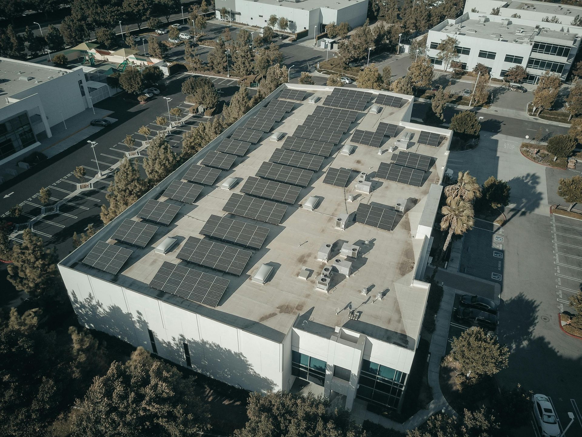 Rooftop solar panels on a large commercial building, surrounded by trees and parking lots.