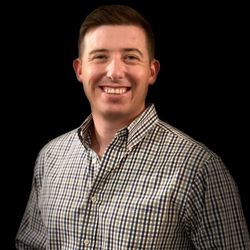 Man smiling at the camera, wearing a button-down shirt, black background.