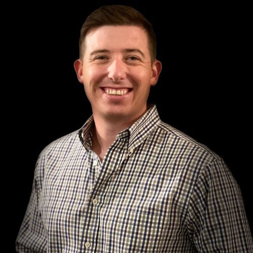 Man smiling at the camera, wearing a button-down shirt, black background.