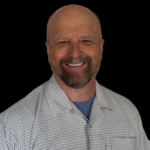 Bald man with a beard, smiling, wearing a button-down shirt over a blue shirt.