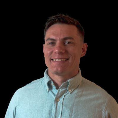 Smiling man in light blue shirt against a black background.