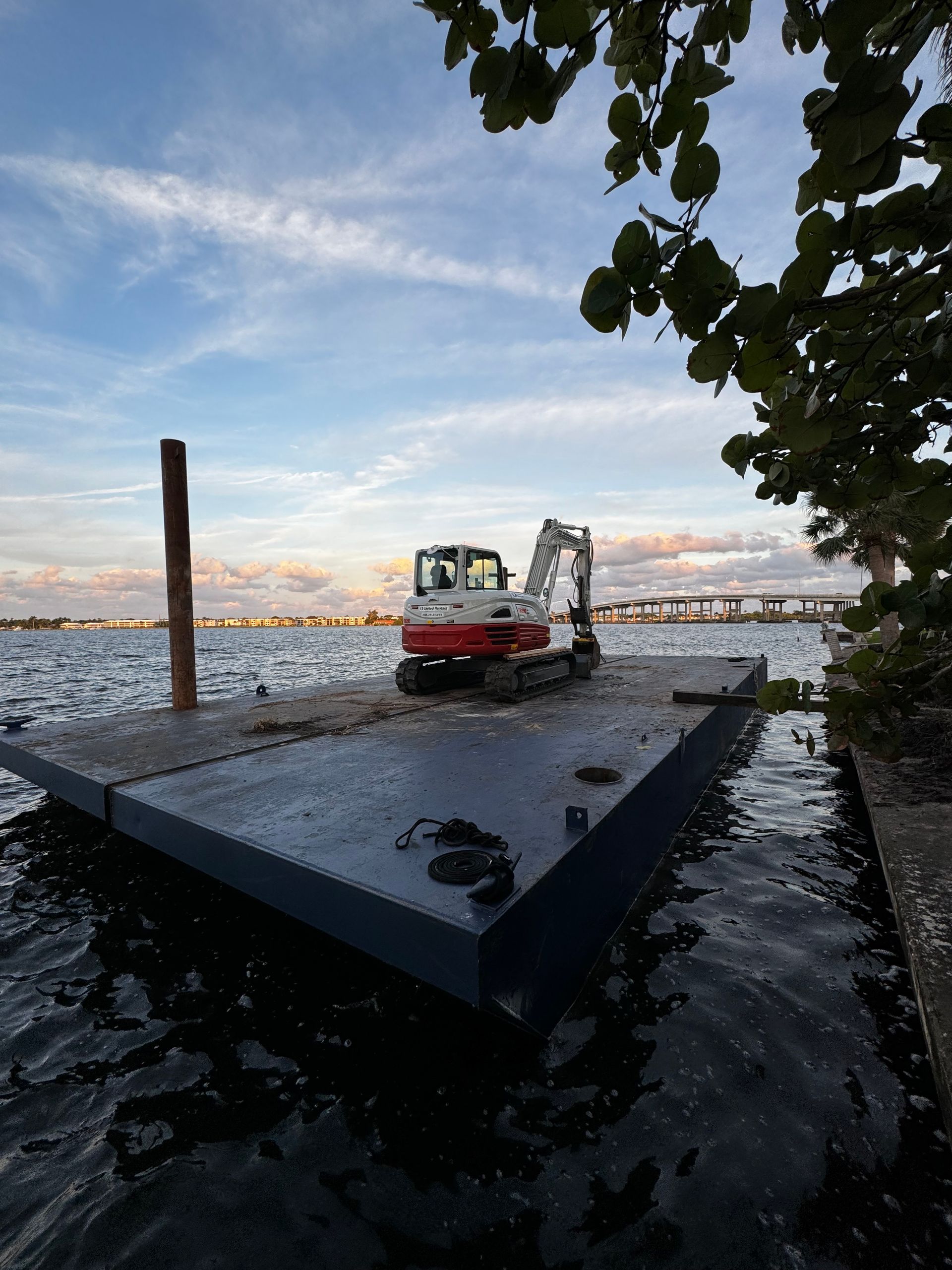 A red and white excavator is parked on a dock in the water.