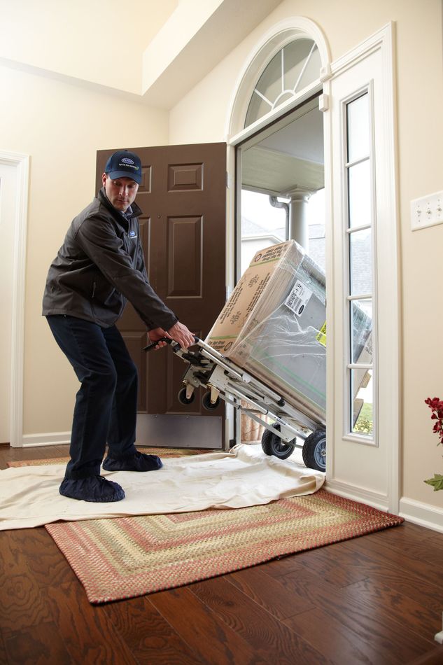 A man is pushing a refrigerator on a dolly into a doorway.