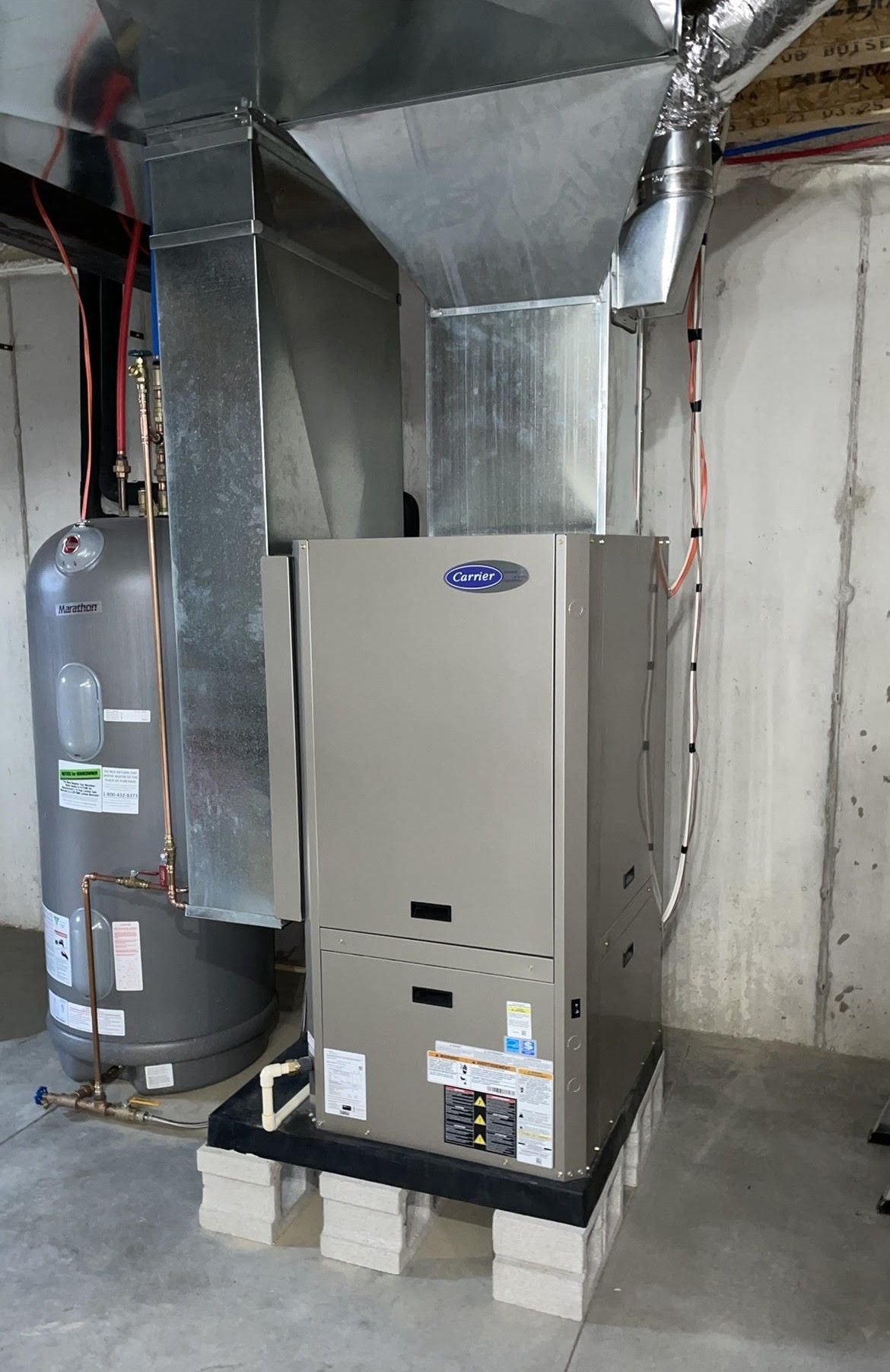 an air conditioner is sitting in a basement next to a water heater .