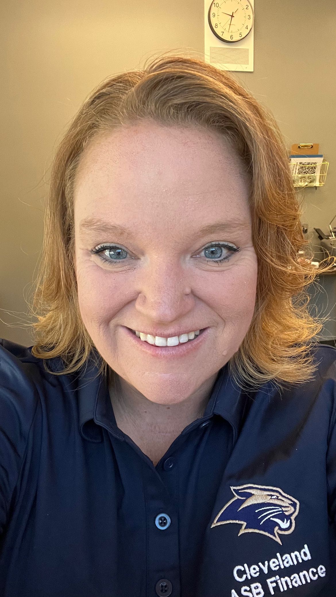 Man in green polo stands on a football field, arms crossed, stadium in background.