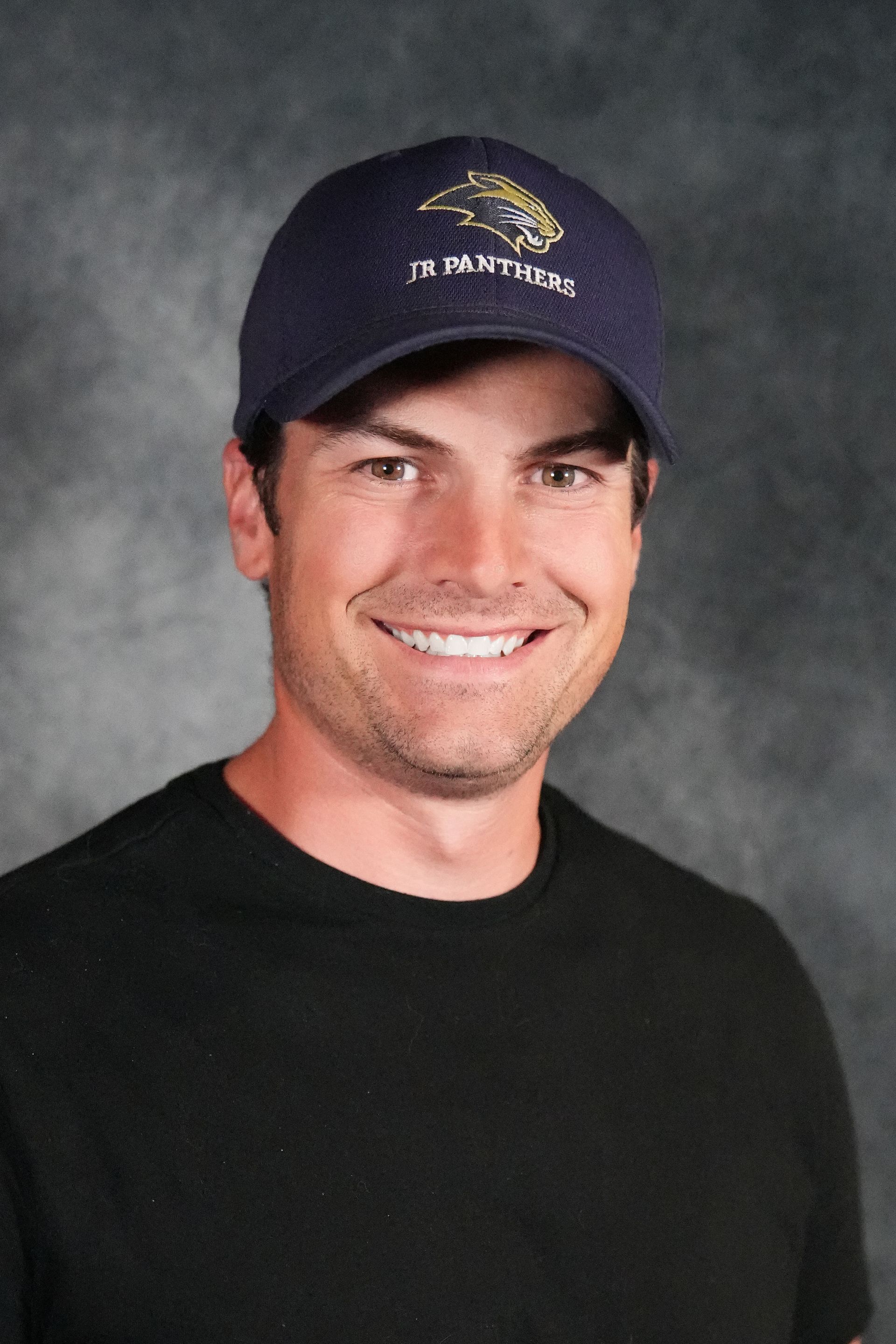 Man with crossed arms on a football field. He is wearing a blue polo shirt, khaki pants, and has a serious expression.