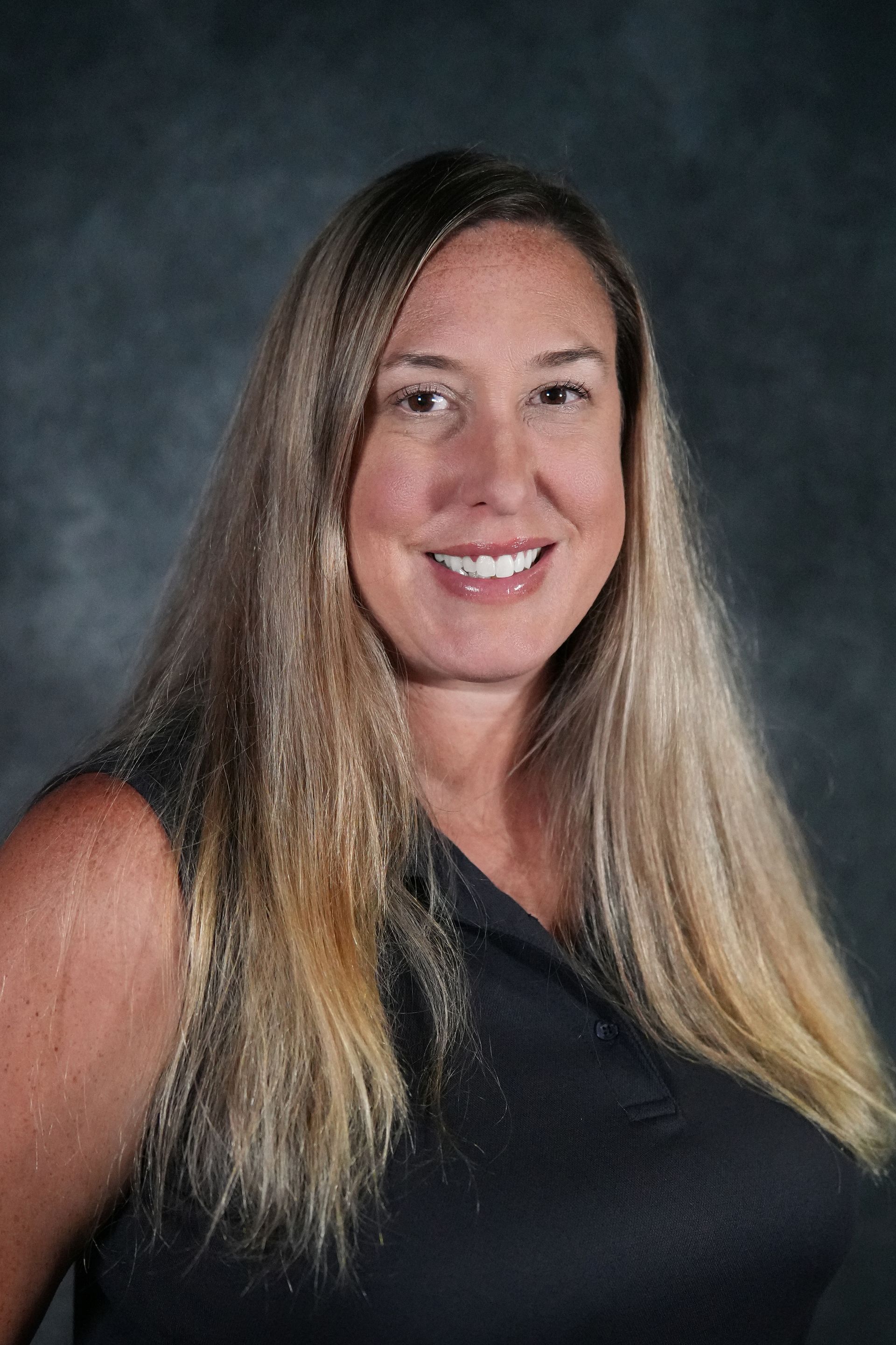 Man in green polo stands on a football field, arms crossed, stadium in background.