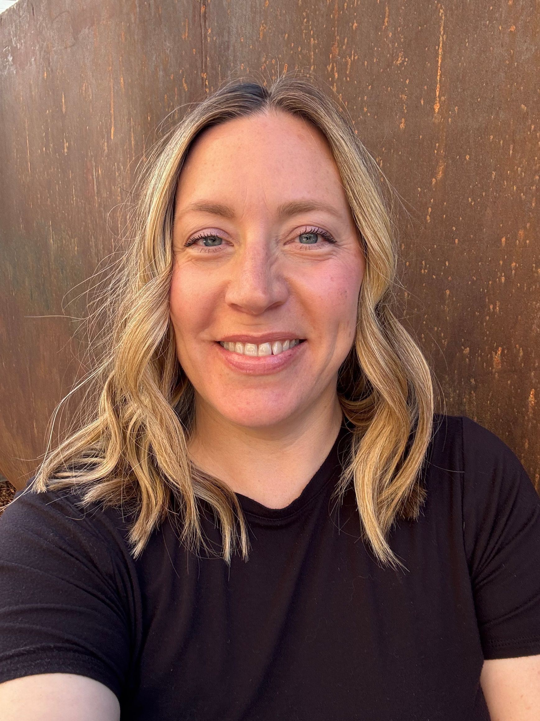 Man with crossed arms on a football field. He is wearing a blue polo shirt, khaki pants, and has a serious expression.