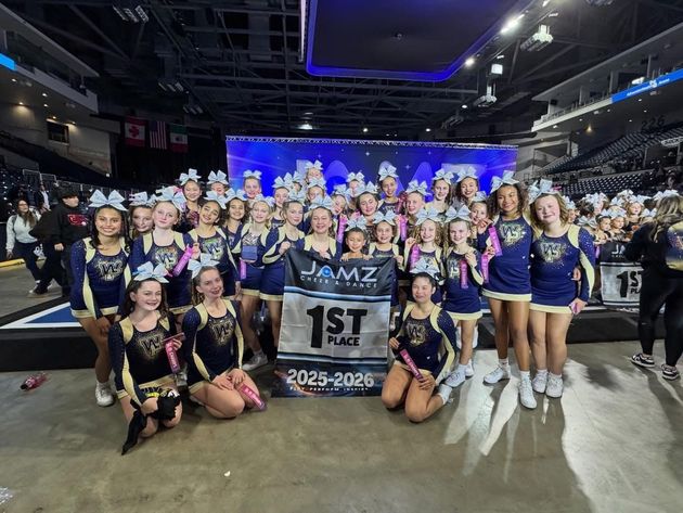 Cheerleader in red uniform performs a backbend on a green and red football field.