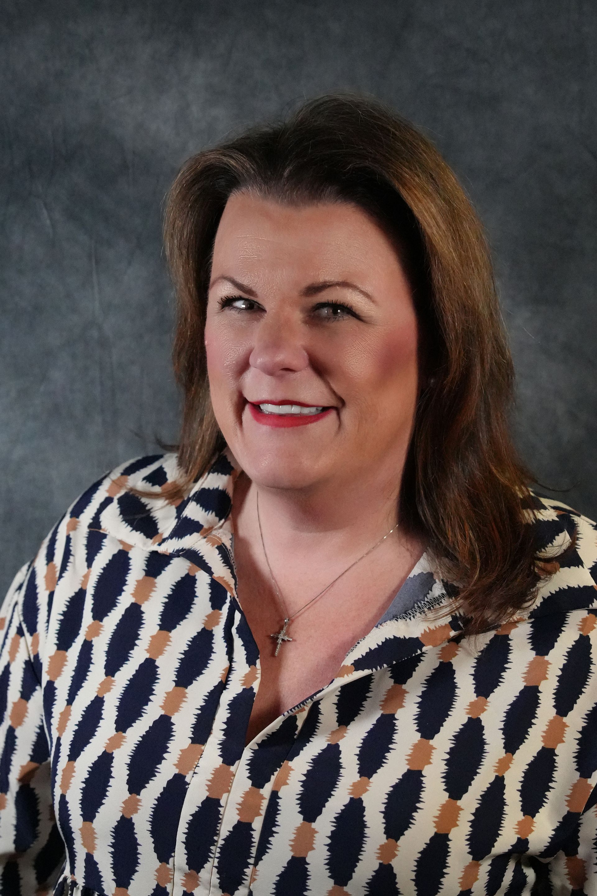 Football coach, arms crossed, on the field. Blue shirt, serious expression, players in background.