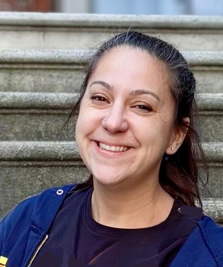 Man in green polo stands on a football field, arms crossed, stadium in background.