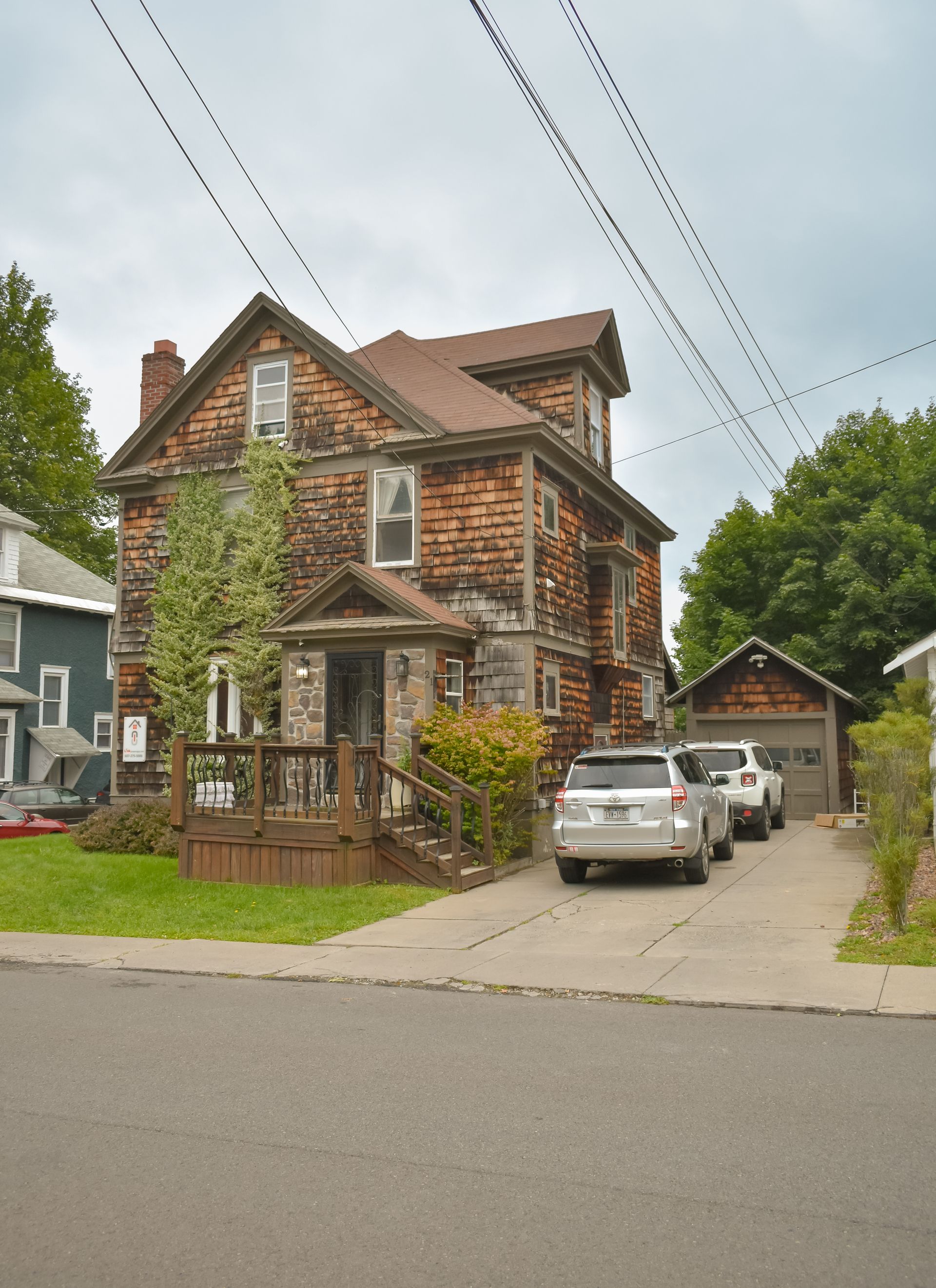 21 Pleasant – Rustic two-story house with stone and shingle exterior, driveway, and small front deck.