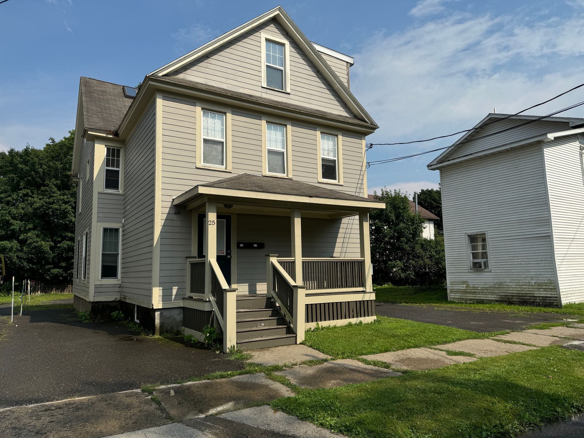 25 Reynolds – Three-story beige house with a covered front porch and a small front yard.