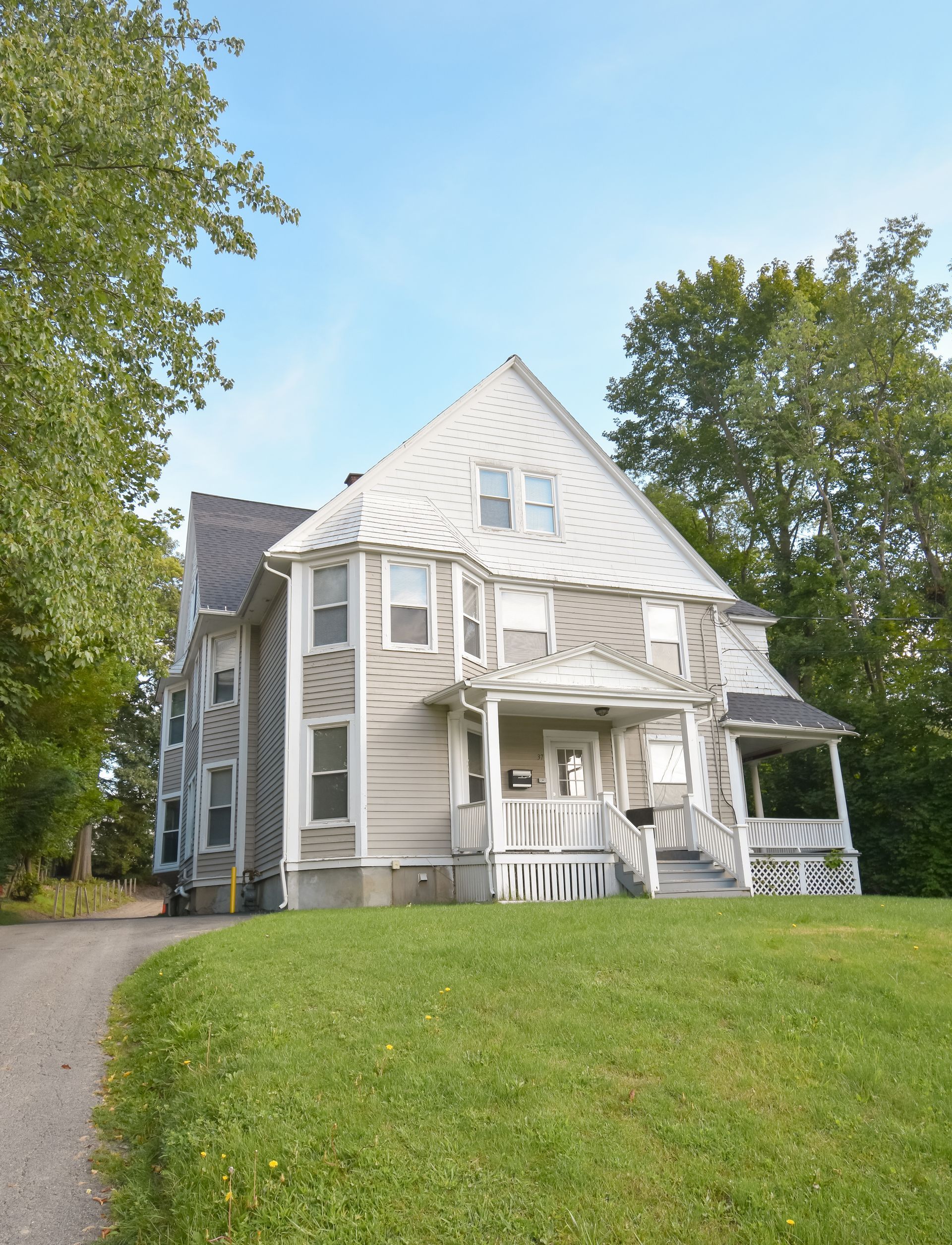 37 Prospect  – Large three-story beige house with front porch, set back from the street with trees in the background.