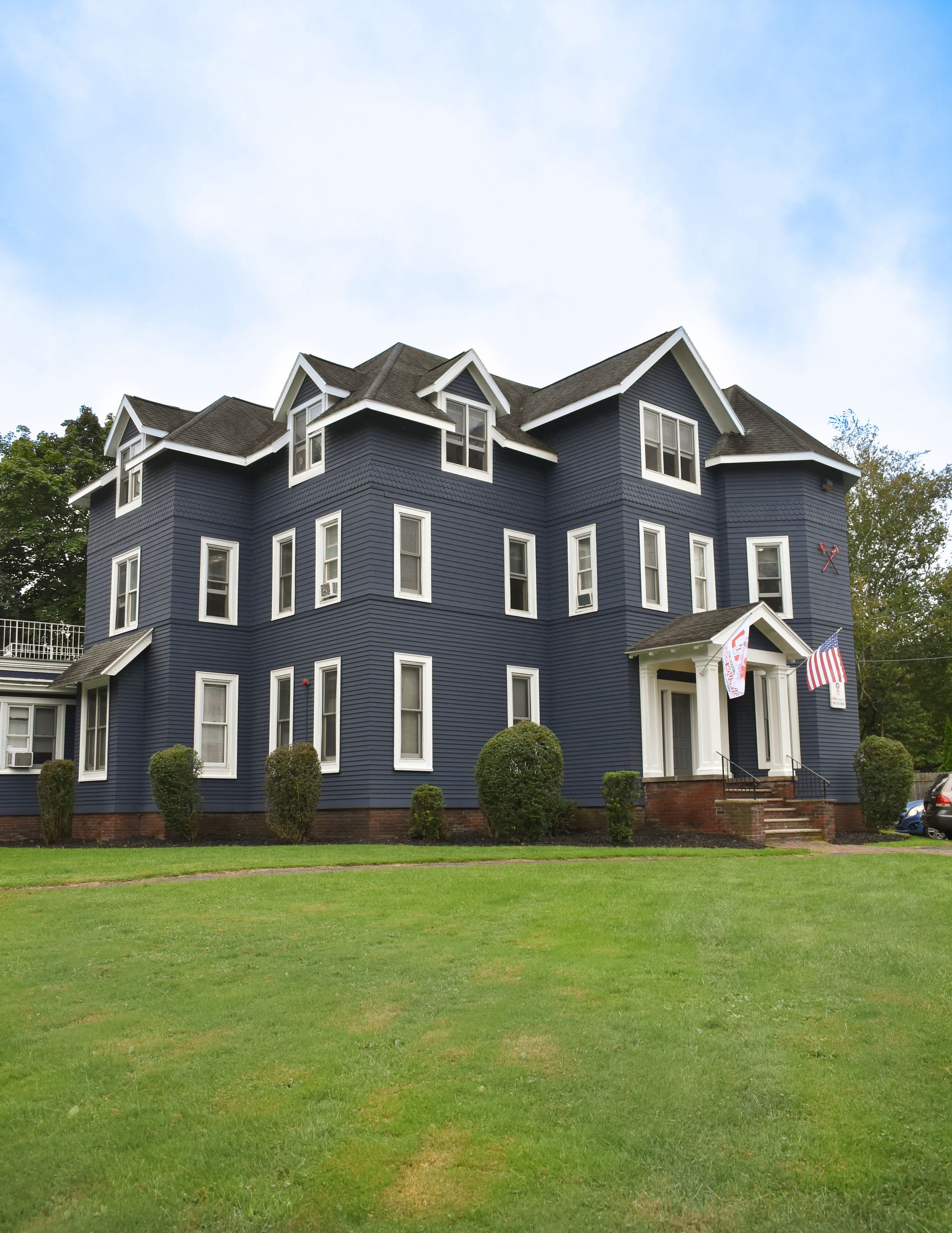 59 Tompkins  – Large navy-blue multi-story house with white trim and American flags at the entrance.