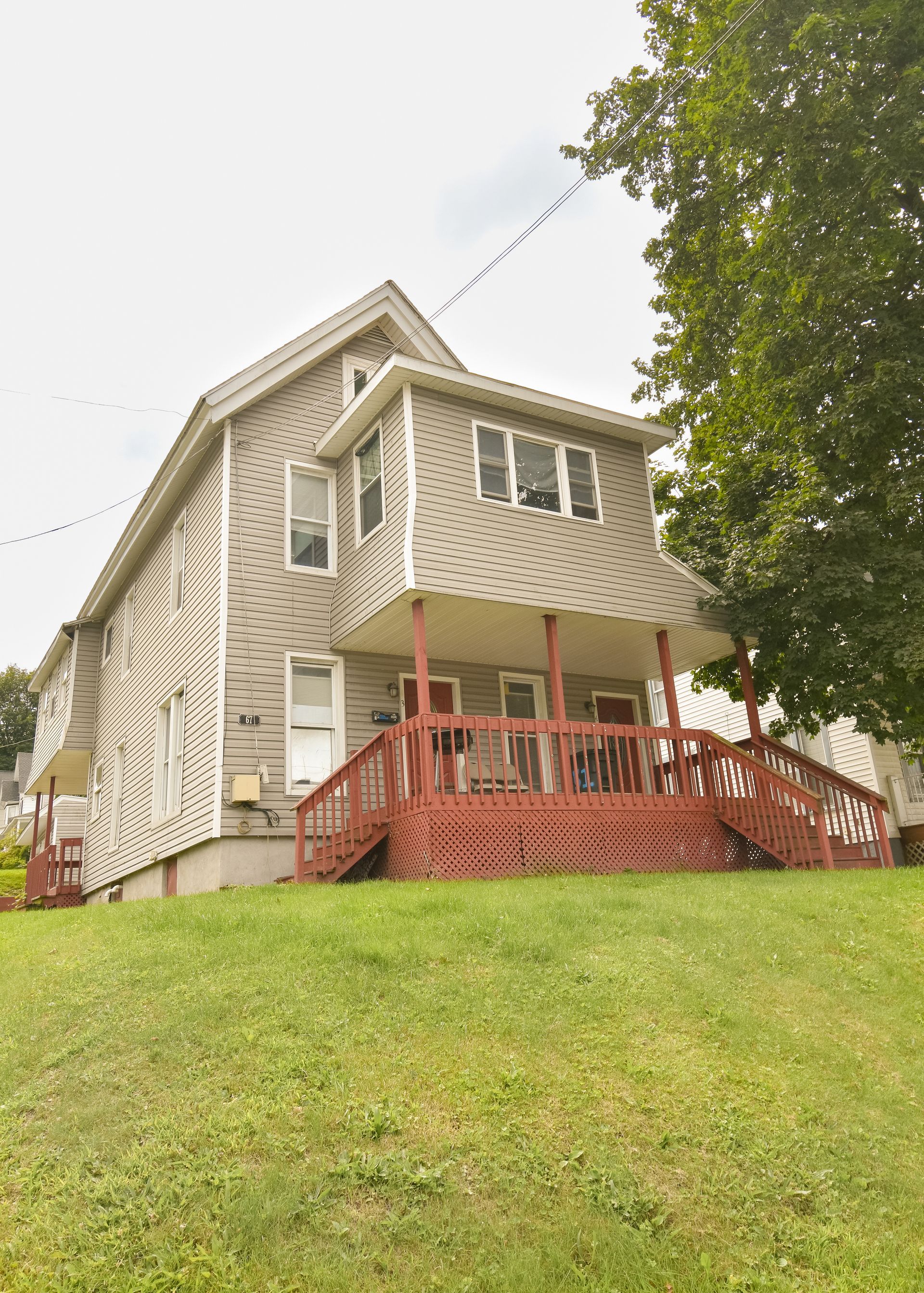 67 Groton – Two-story beige house with red front porch and railing, situated on a grassy lot.