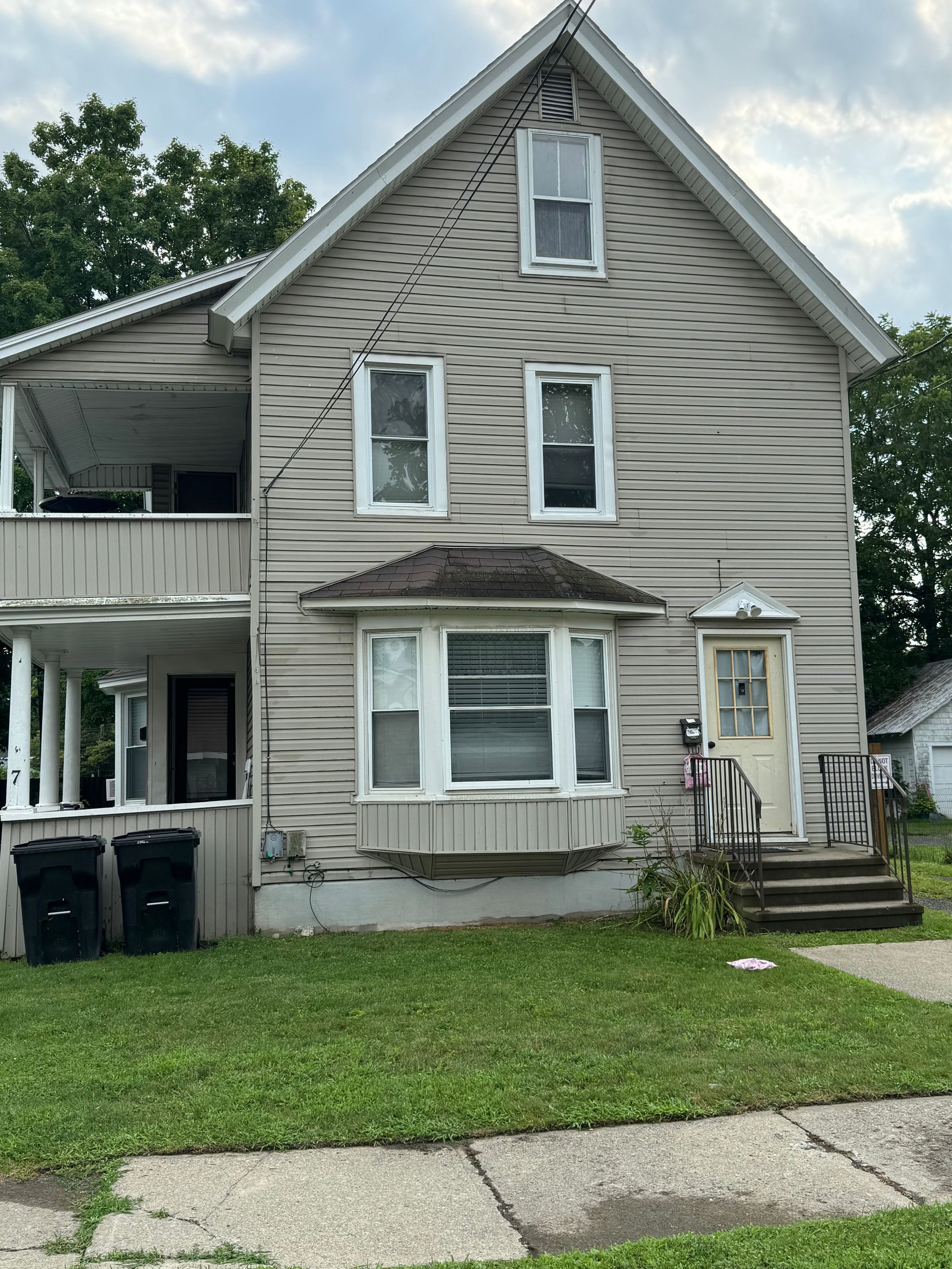 7 Water Street – Two-story beige house with front porch steps and garbage bins in front.