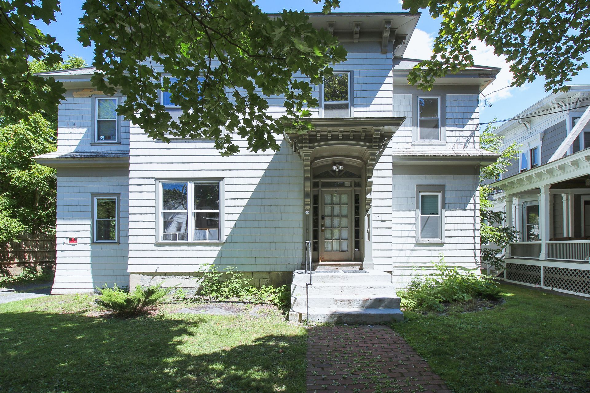 9 Reynolds – Two-story light blue house with an arched front entryway and landscaped front yard.