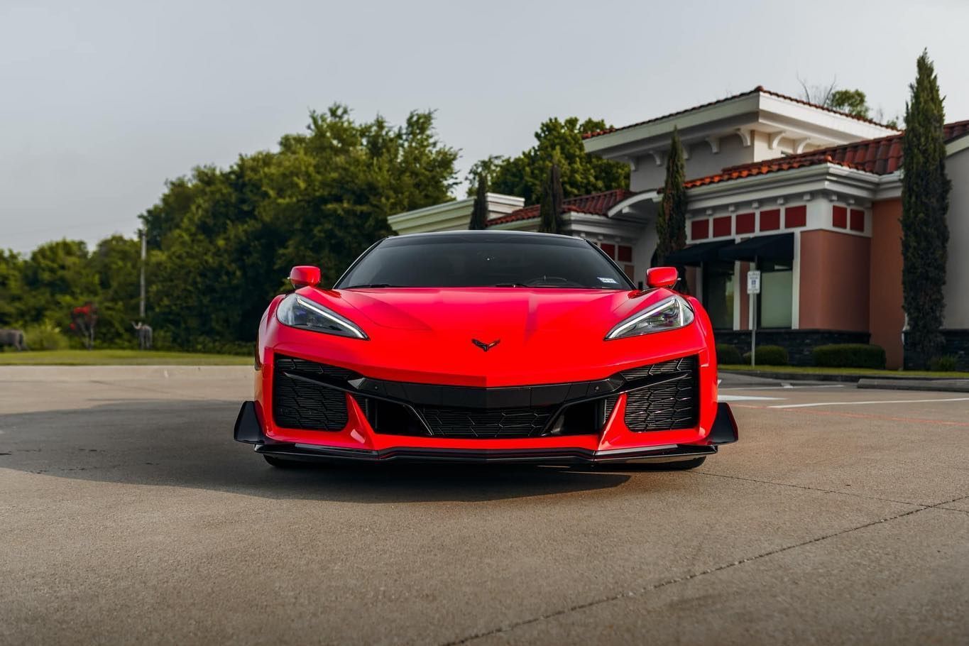 A bright red Chevrolet Corvette sports car parked in front of a building on a sunny day.