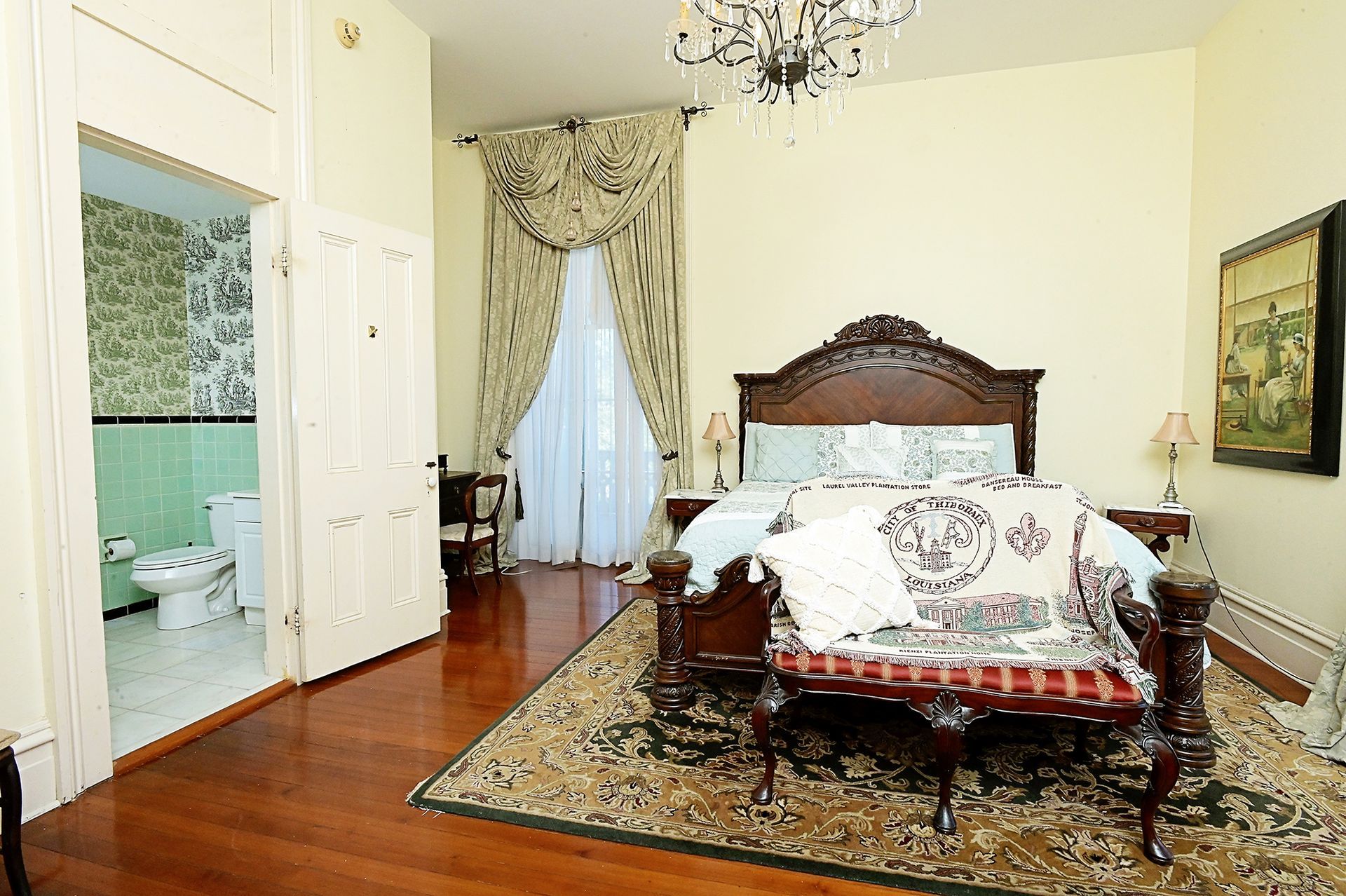 Ornate bedroom with wood floors, bed, rug, and a bathroom door on the left.