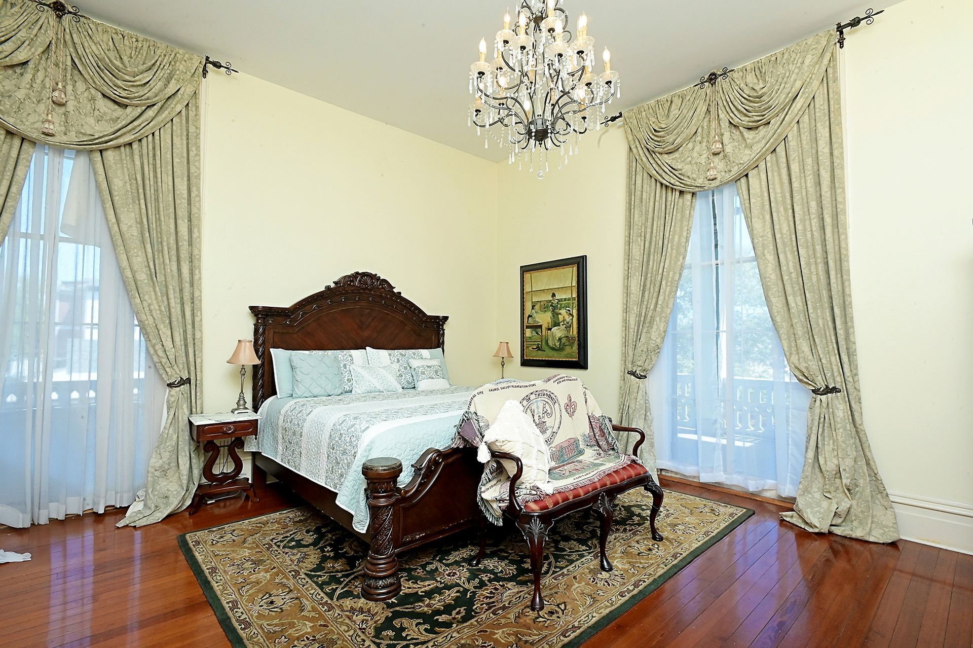 Elegant bedroom with carved bed, ornate curtains, chandelier, and wooden floors.