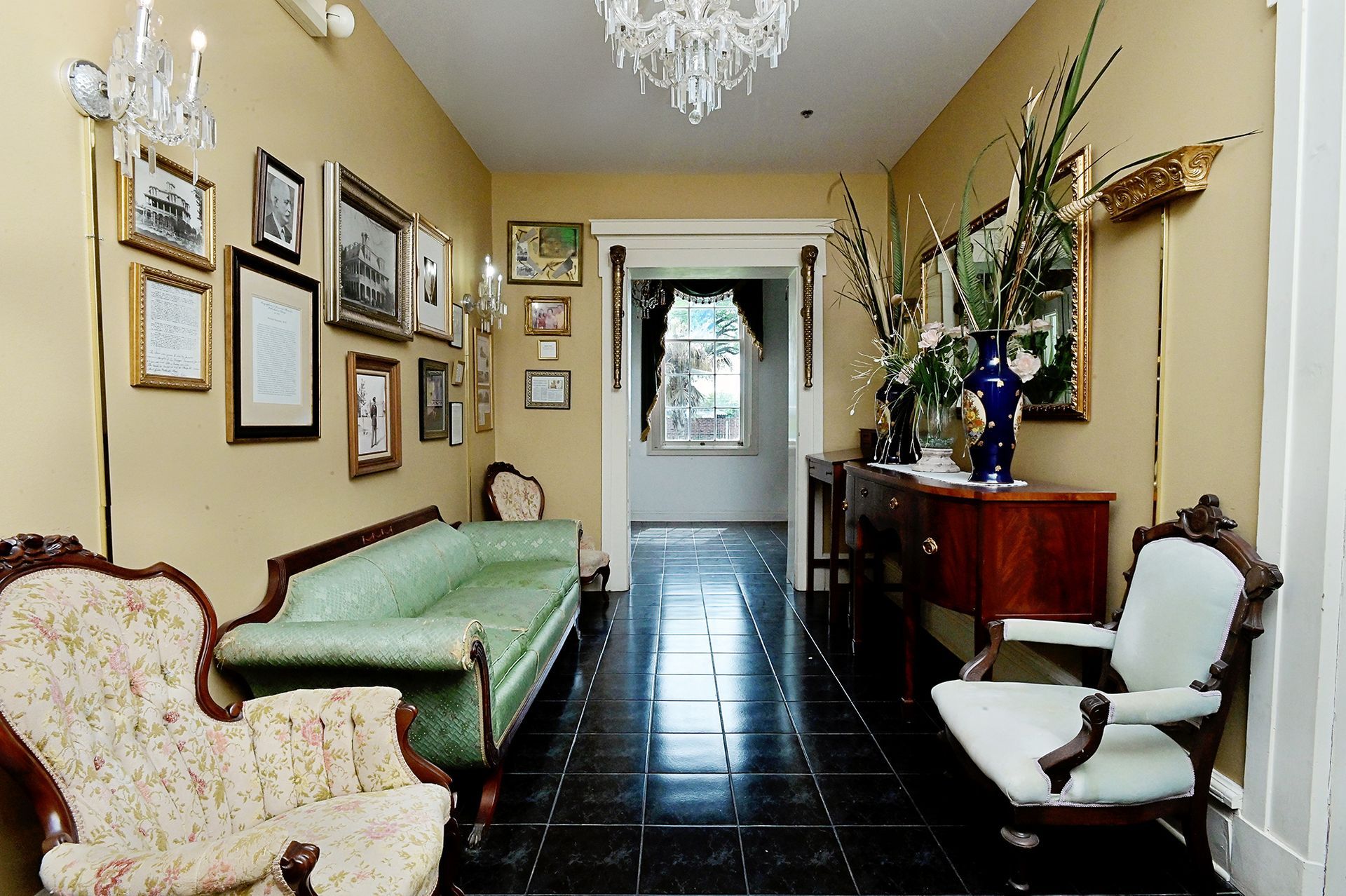 Long hallway with vintage furniture, framed photos, and a chandelier.