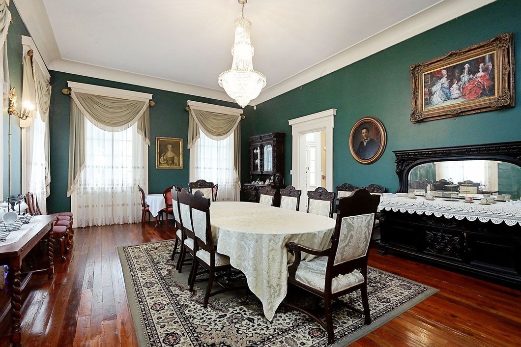 Formal dining room with dark green walls, ornate furniture, and a chandelier.