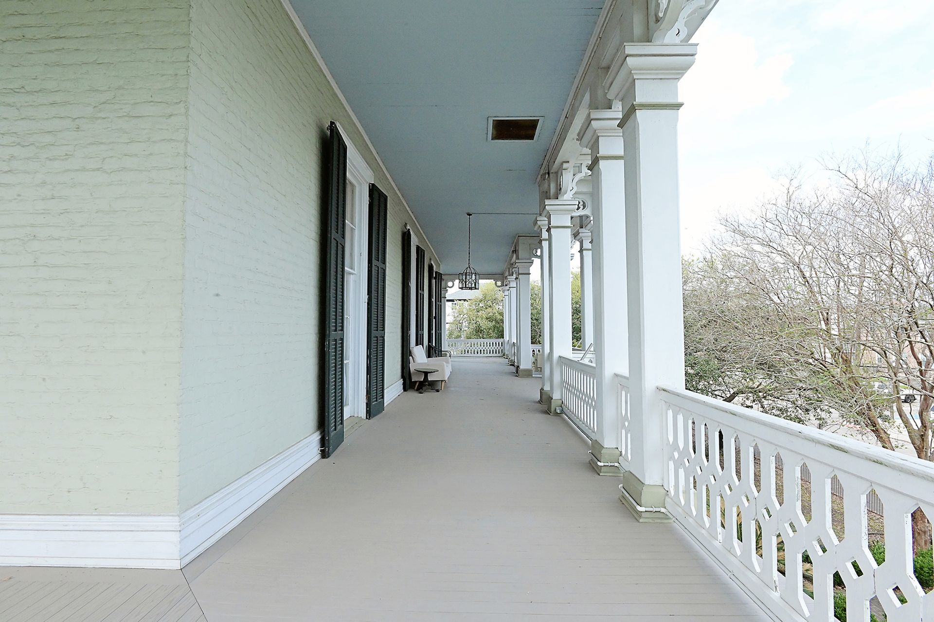 Long porch of a historic building with white columns and railings, shutters, and a light blue ceiling.