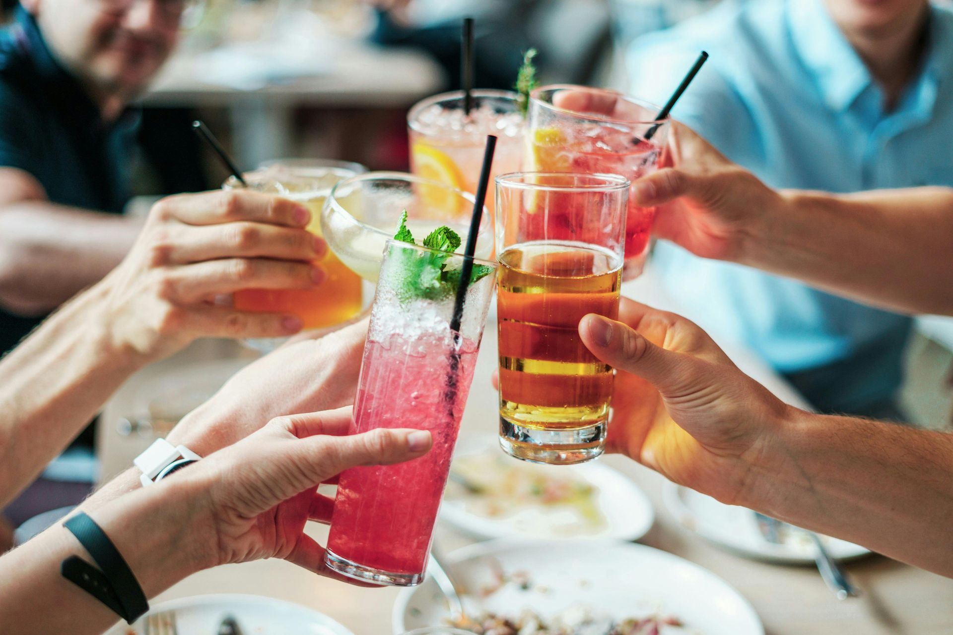 People toasting with colorful cocktails at a restaurant table.