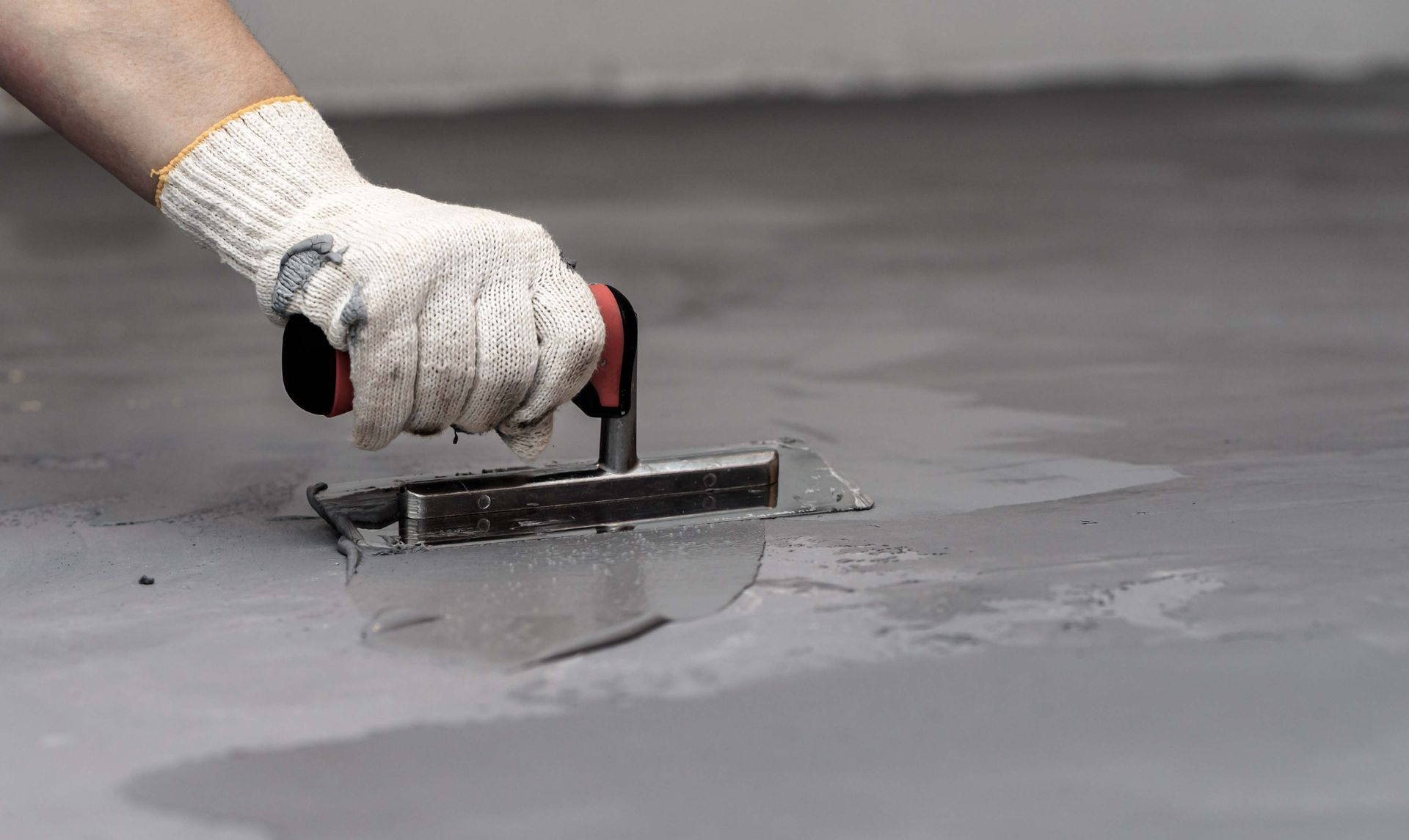 A person is plastering a concrete floor with a trowel.