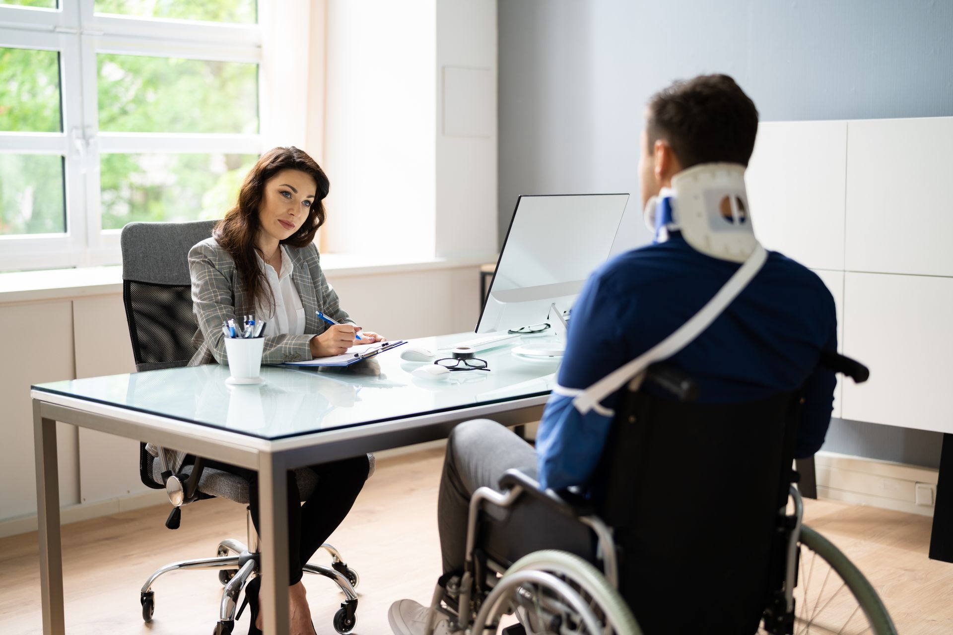 A social security disability lawyer meeting with a client in a wheelchair at an office desk.